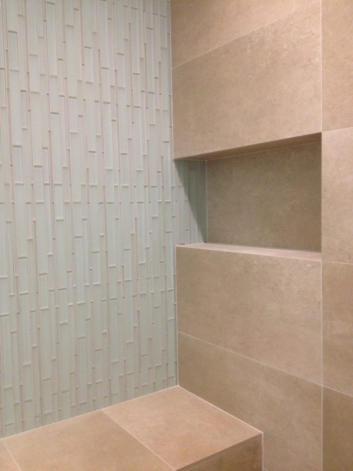 Glass-mosaic accent wall beside a porcelain-tiled shower niche and bench in a Beverly Hills bathroom by Accelerate Construction