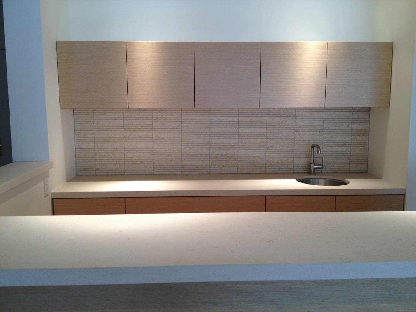The finished Brentwood wet bar with rift-cut white-oak cabinetry, a travertine backsplash and concealed lighting