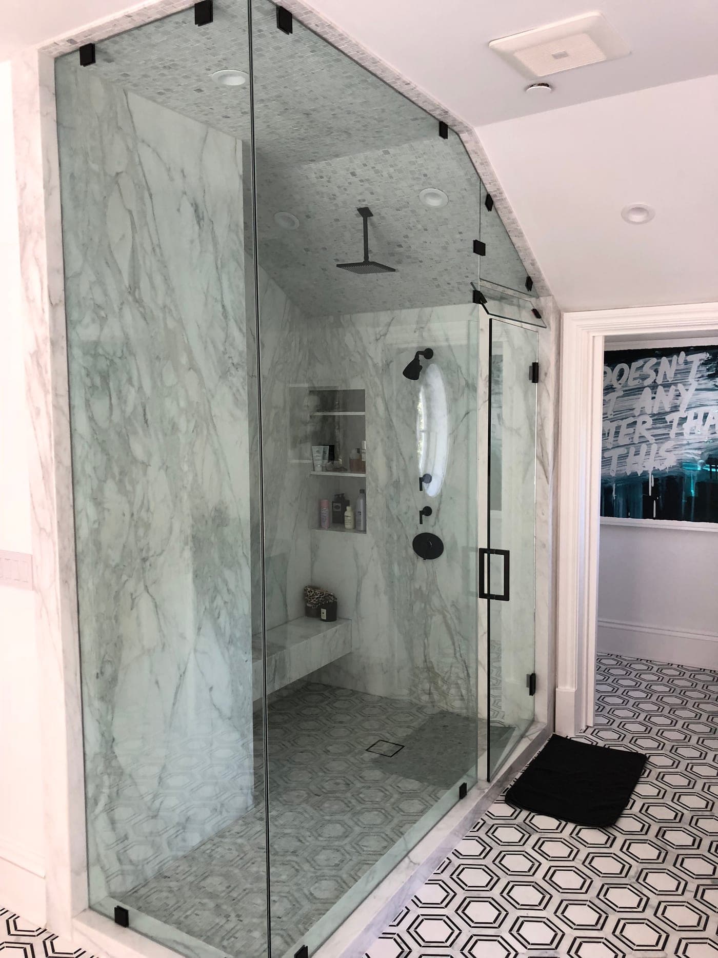 Pacific Palisades master bath by Accelerate Construction: a frameless-glass steam shower in book-matched Calacatta marble with a built-in bench, over a black-and-white hex-tile floor