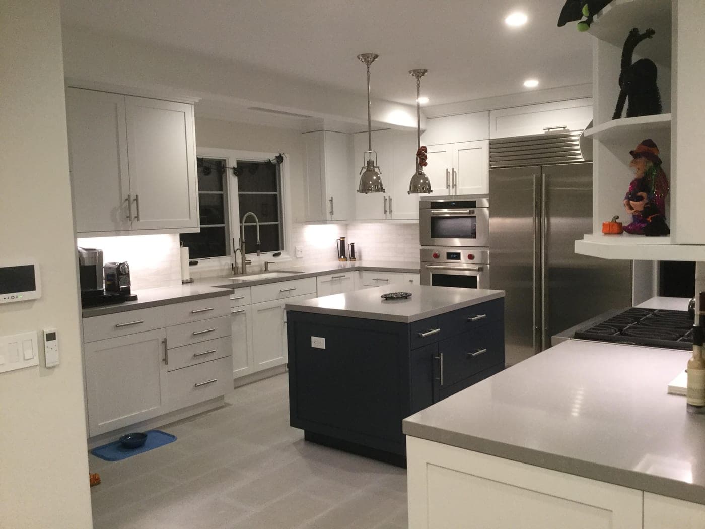 Pacific Palisades kitchen by Accelerate Construction with white shaker cabinetry, a navy island, quartz counters and professional stainless appliances