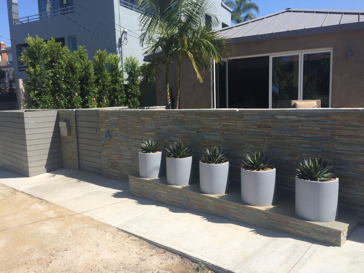 The rebuilt Playa del Rey exterior with a stacked-stone retaining wall, planters and a standing-seam metal roof