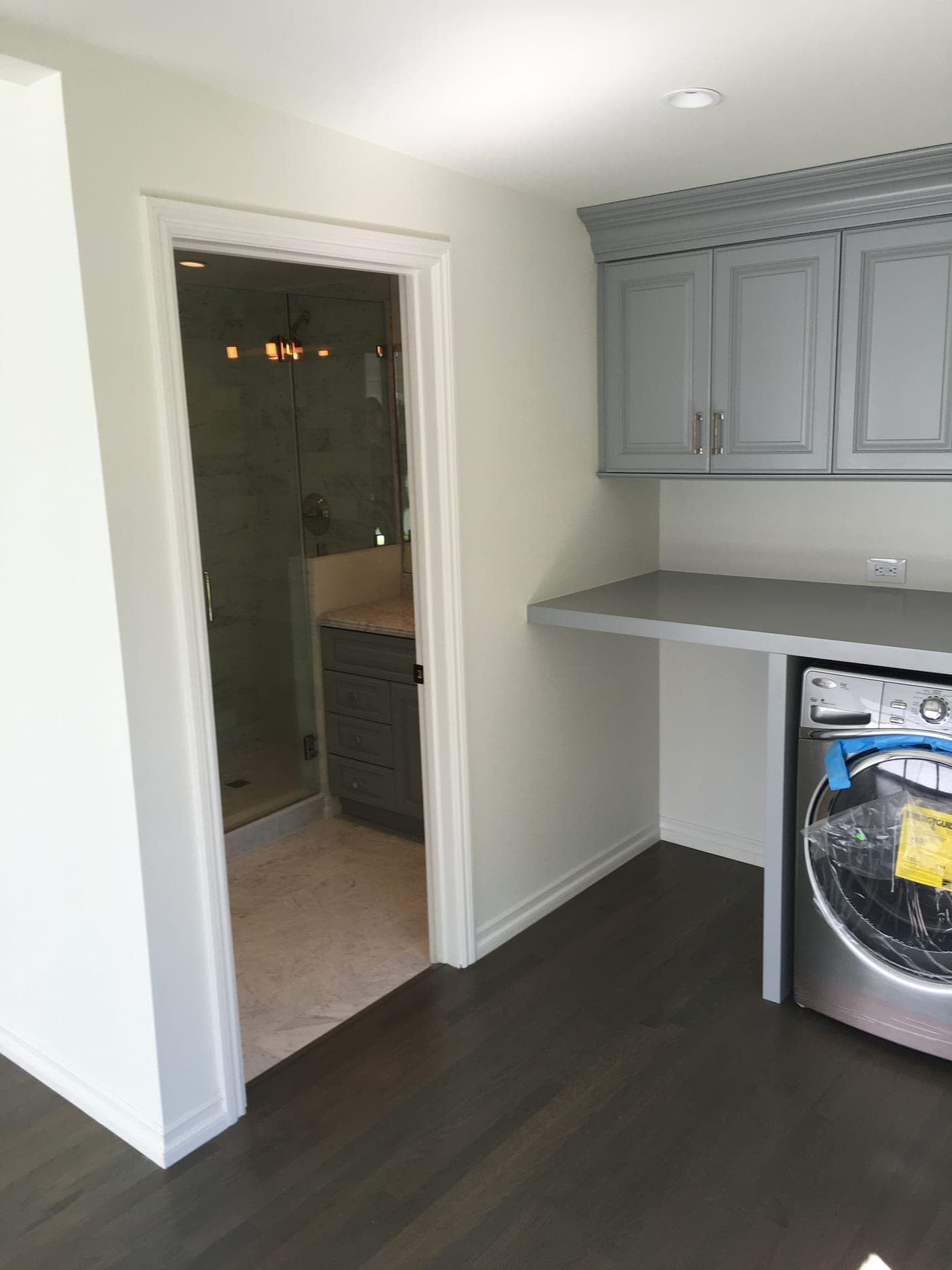 Finished interior of the rebuilt West Hollywood garage: a laundry counter with gray cabinetry and a doorway to the marble bathroom with its glass shower