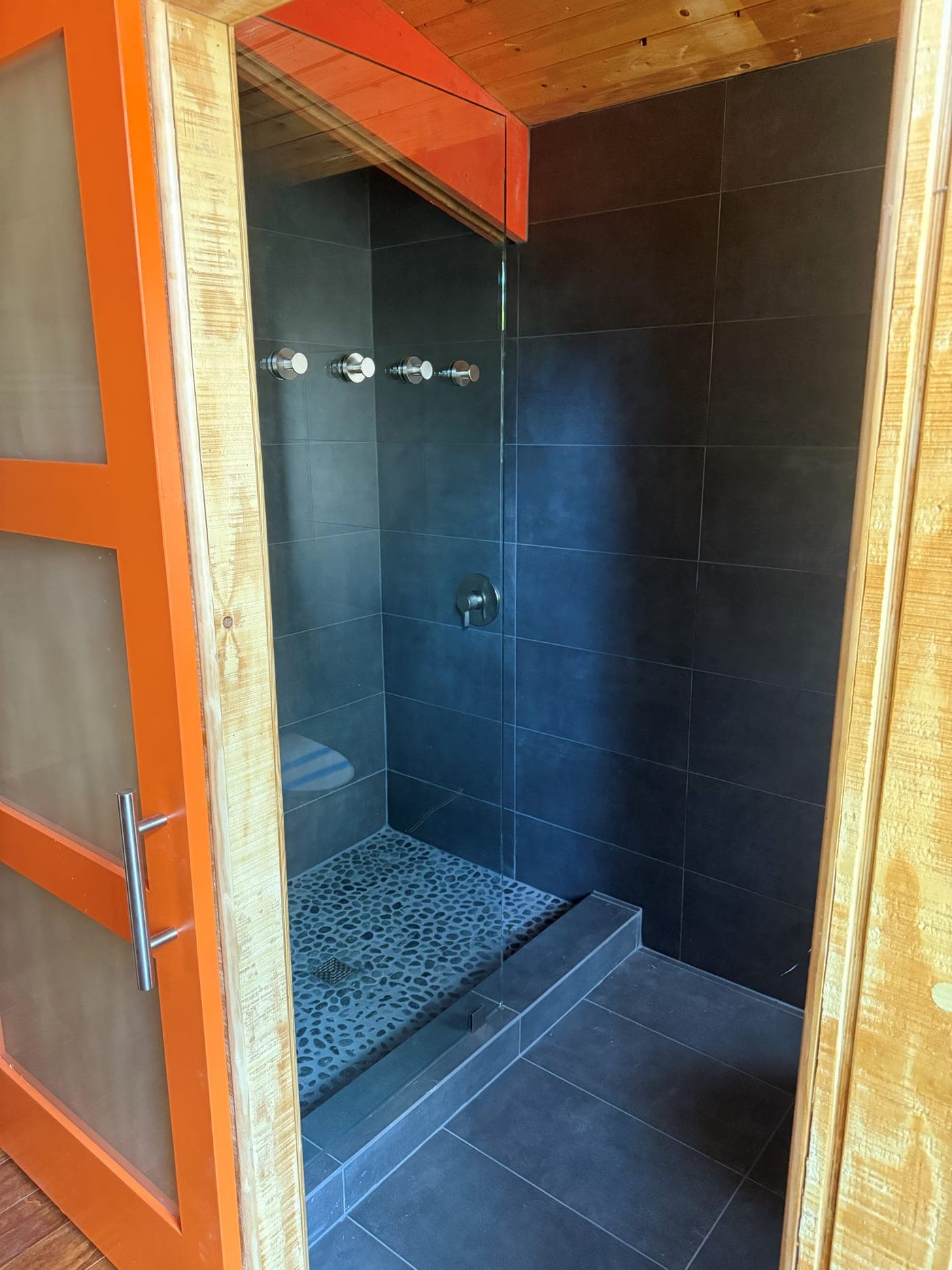 New bathroom of the Wrightwood renovation with a dark-tiled shower behind an orange-framed glass door