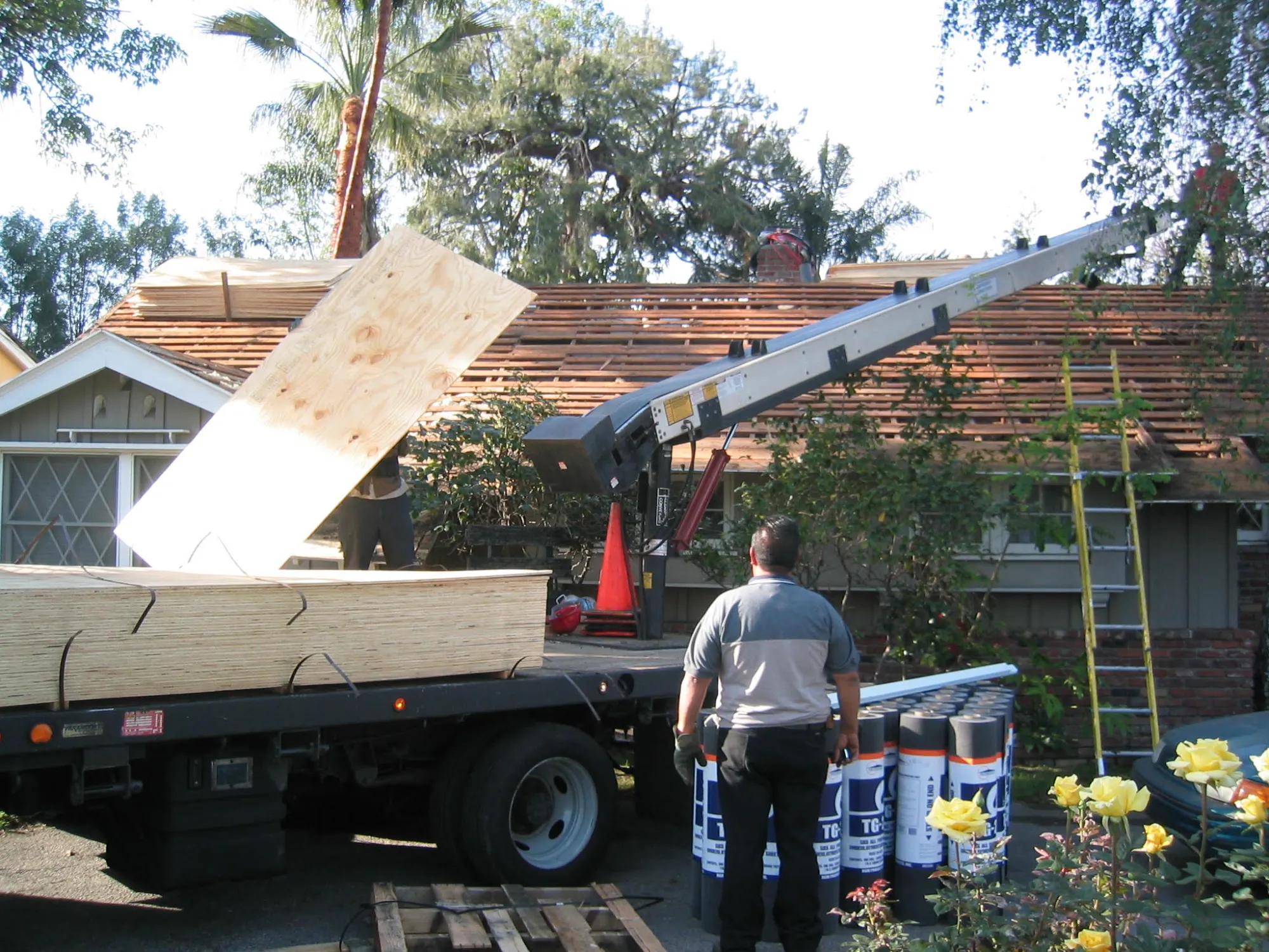 The Los Angeles home's old wood-shake roof stripped to the spaced boards while new plywood sheathing is sent up to the roof by conveyor